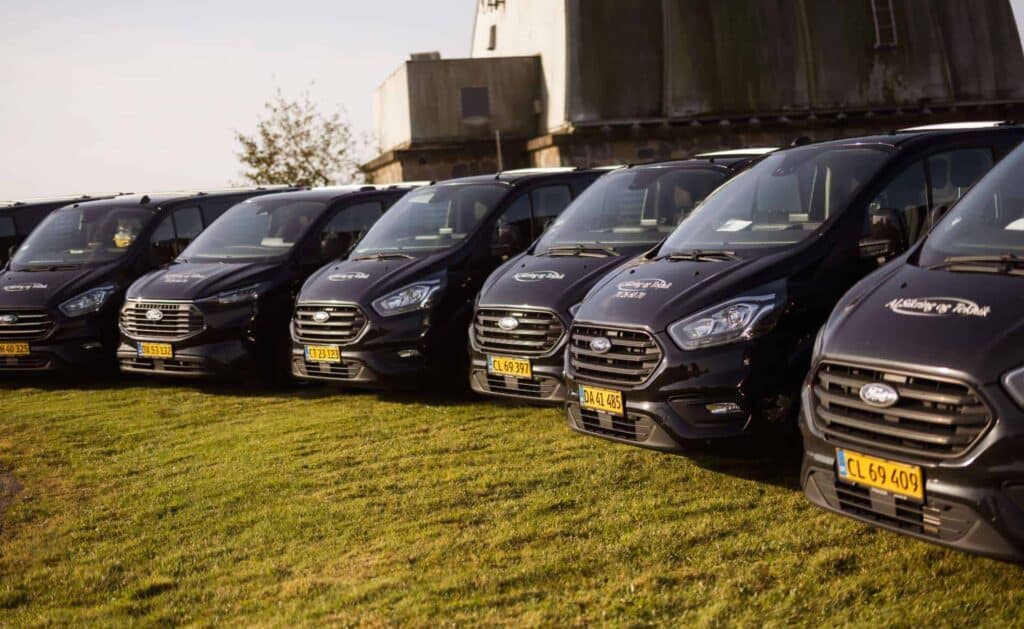 Seks firmabiler fra AJ Sikring og Teknik parkeret på græsplæne