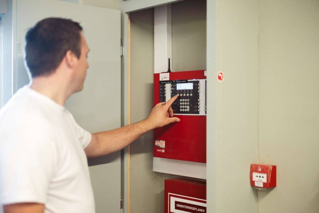 Elektriker betjener stor rød brandalarm og sikrer optimal drift i et skab